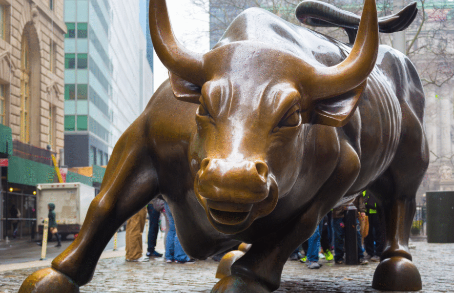 Charging Bull sculpture on Wall Street framed by summer sunlight with a slight sun flare, symbolizing market momentum.