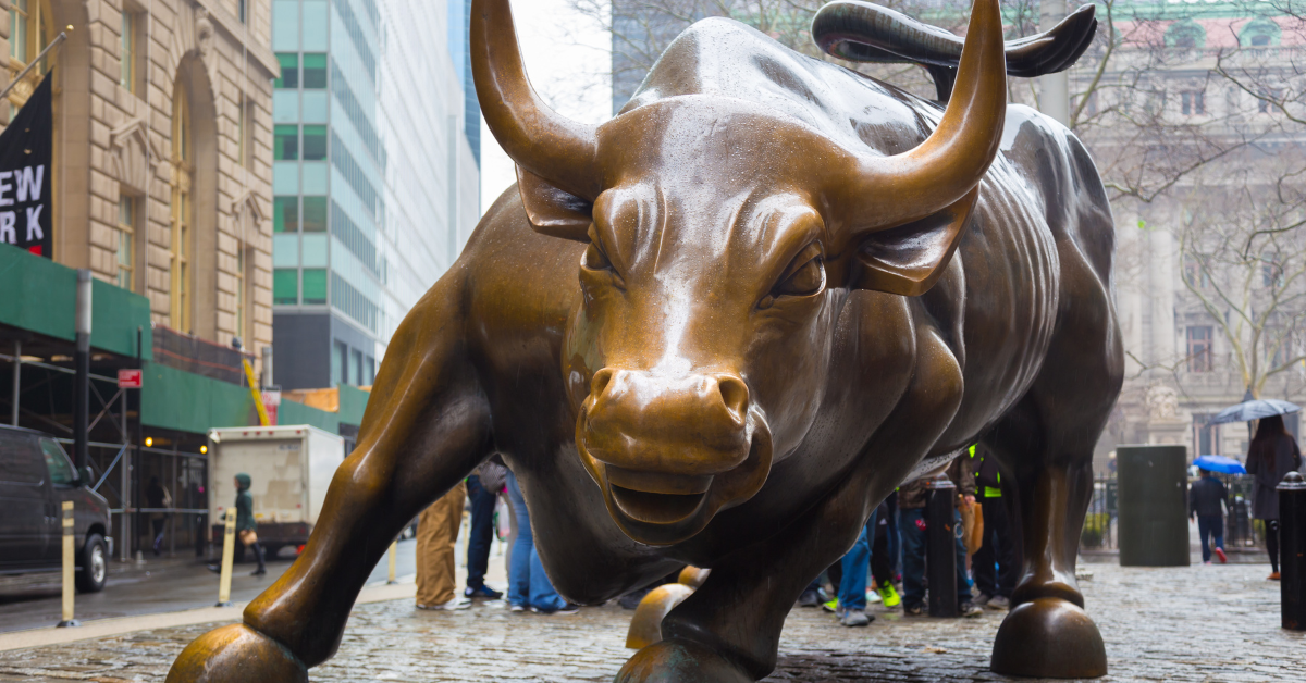 Charging Bull sculpture on Wall Street framed by summer sunlight with a slight sun flare, symbolizing market momentum.