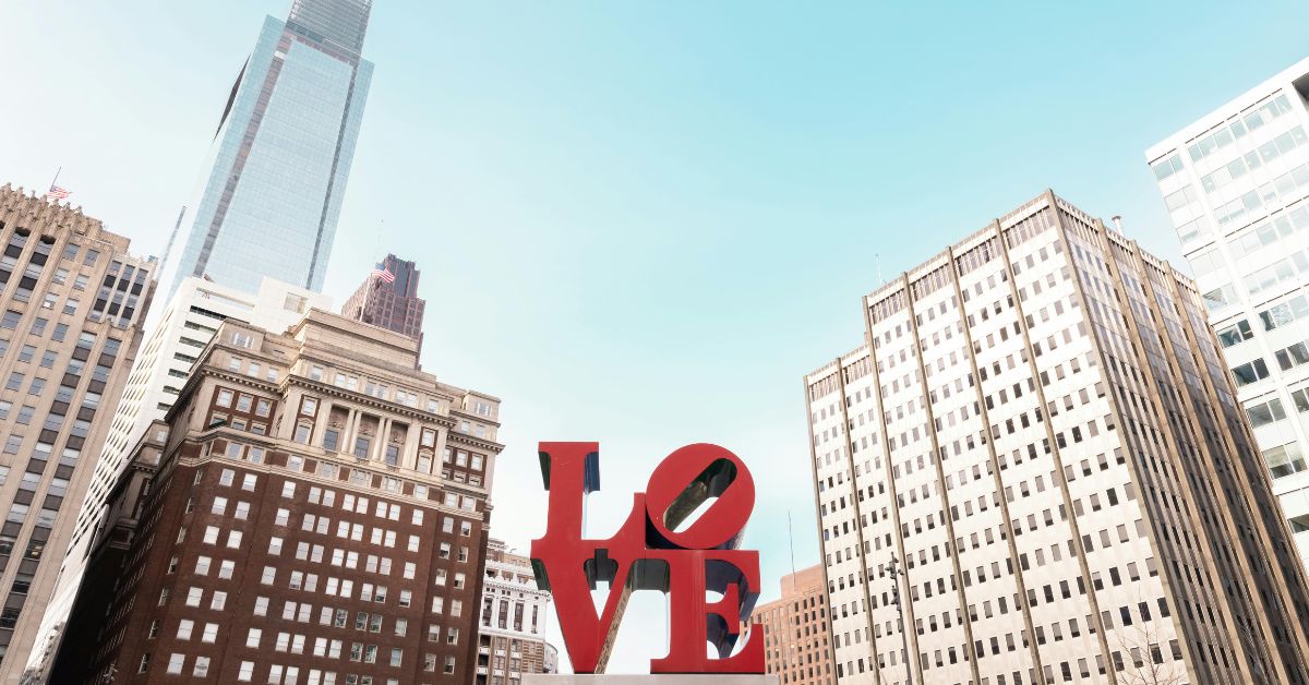 Philadelphia LOVE sculpture in Center City surrounded by historic and modern office buildings under a clear blue sky.